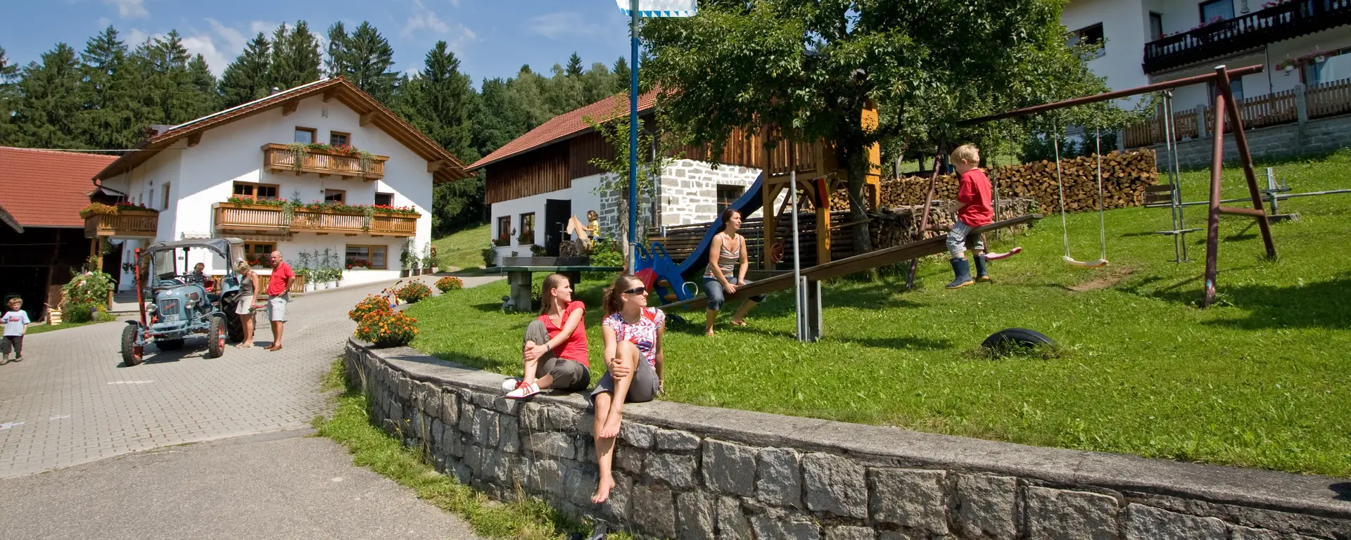 ein Hofgelände mit Ferienhaus, Stallgebäude  und Wohnhaus, Spielplatz und Traktor  