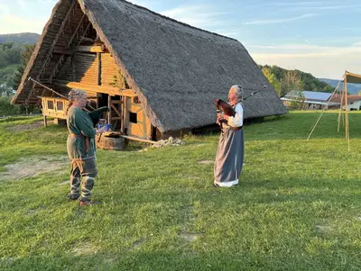 zwei Frauen in historischen Gewändern spielen Dudelsack vor einer einfachen Holzbehausung im Keltendorf 