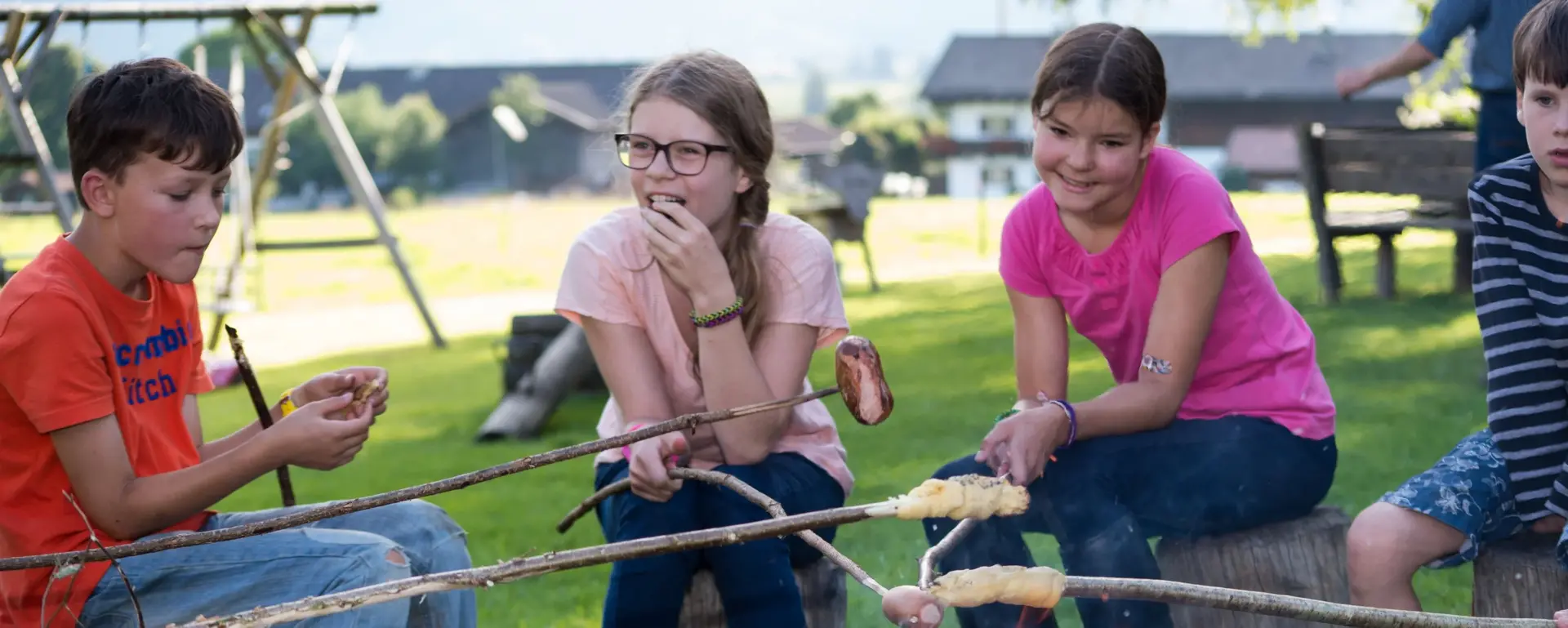 Kinder sitzen abends am Lagerfeuer und grillen Stockbrot 