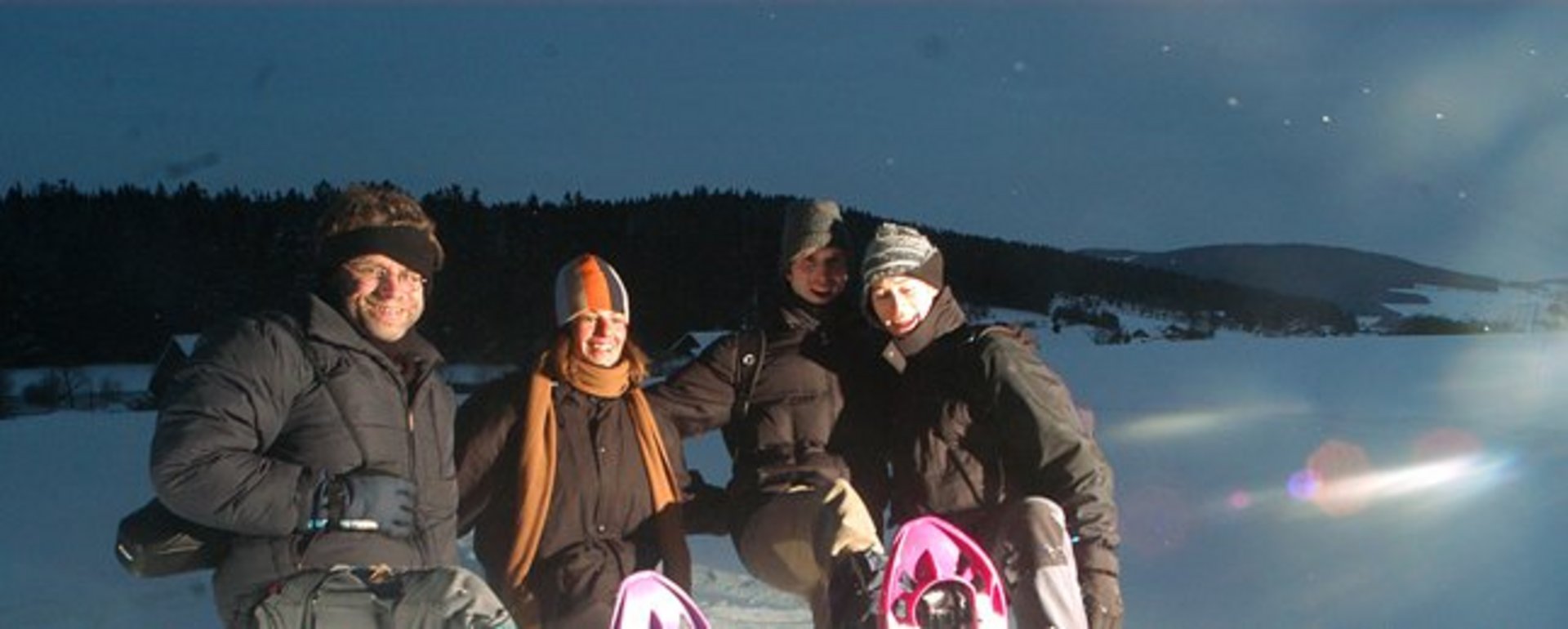 Gruppe von Schneeschuhwanderer mit Stirnlampen unterwegs durch die nächtliche Schneelandschaft 