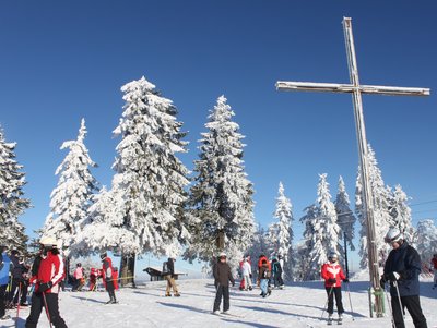 reges Getummel am Gipfelkreuz im Skizentrum Mittedorf-Philippsreut mit Skifahrer, Schneeschuhgeher, Rodler 